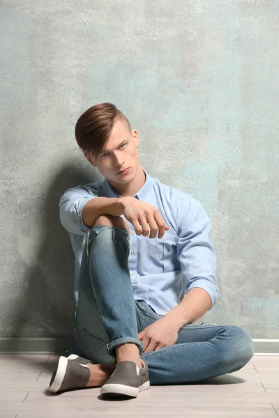 Schöner junger Mann sitzt auf dem Boden in der Nähe einer strukturierten Wand — Stockfoto