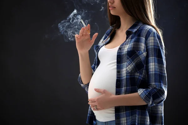 Беременная женщина курит сигарету на тёмном фоне — стоковое фото