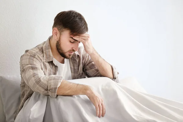 Mladý muž s bolestí hlavy, sedící na posteli — Stock fotografie