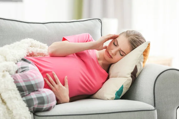 Mulher grávida que sofre de dores de cabeça enquanto deitada no sofá em casa — Fotografia de Stock