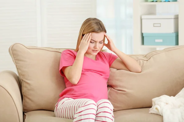 Беременная женщина, страдающая от головной боли, сидя дома на диване — стоковое фото
