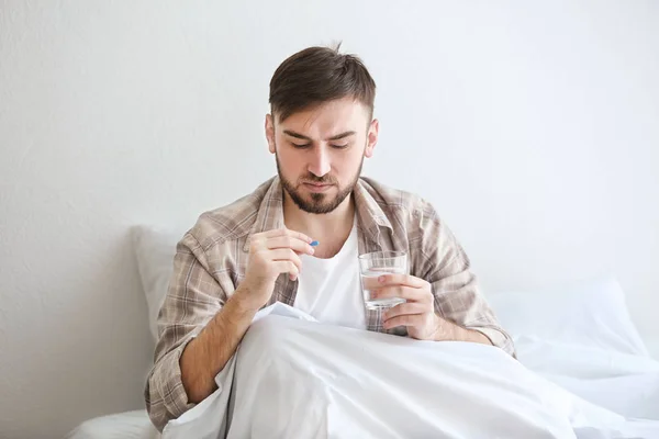 Jovem sentado na cama e tomando pílula — Fotografia de Stock