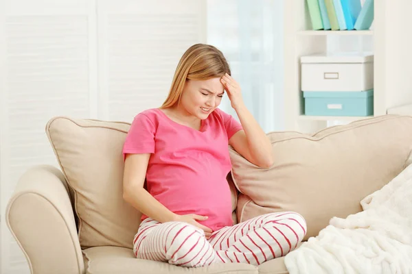 Femeie gravidă care suferă de dureri de cap în timp ce stă pe canapea acasă — Fotografie, imagine de stoc