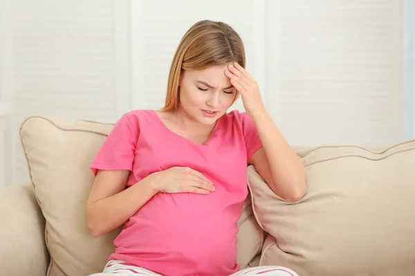 Mujer embarazada que sufre de dolores de cabeza mientras está sentada en el sofá en casa — Foto de Stock