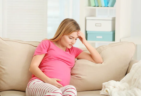 Gravid kvinne med hodepine mens hun sitter på sofaen hjemme – stockfoto