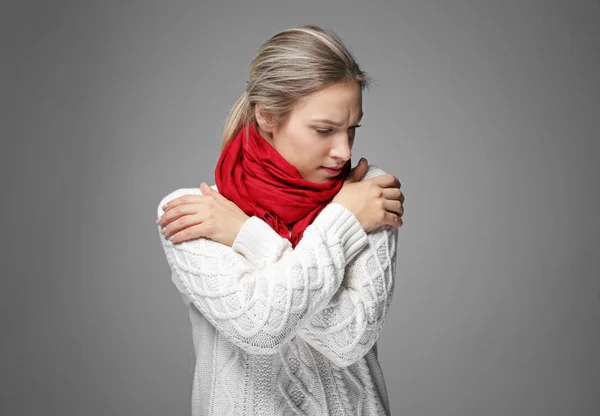 Young woman in warm clothes shivering from cold on gray background — Stock Photo, Image