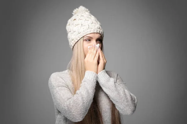 Mujer joven usando tejido para sonarse la nariz sobre fondo gris —  Fotos de Stock