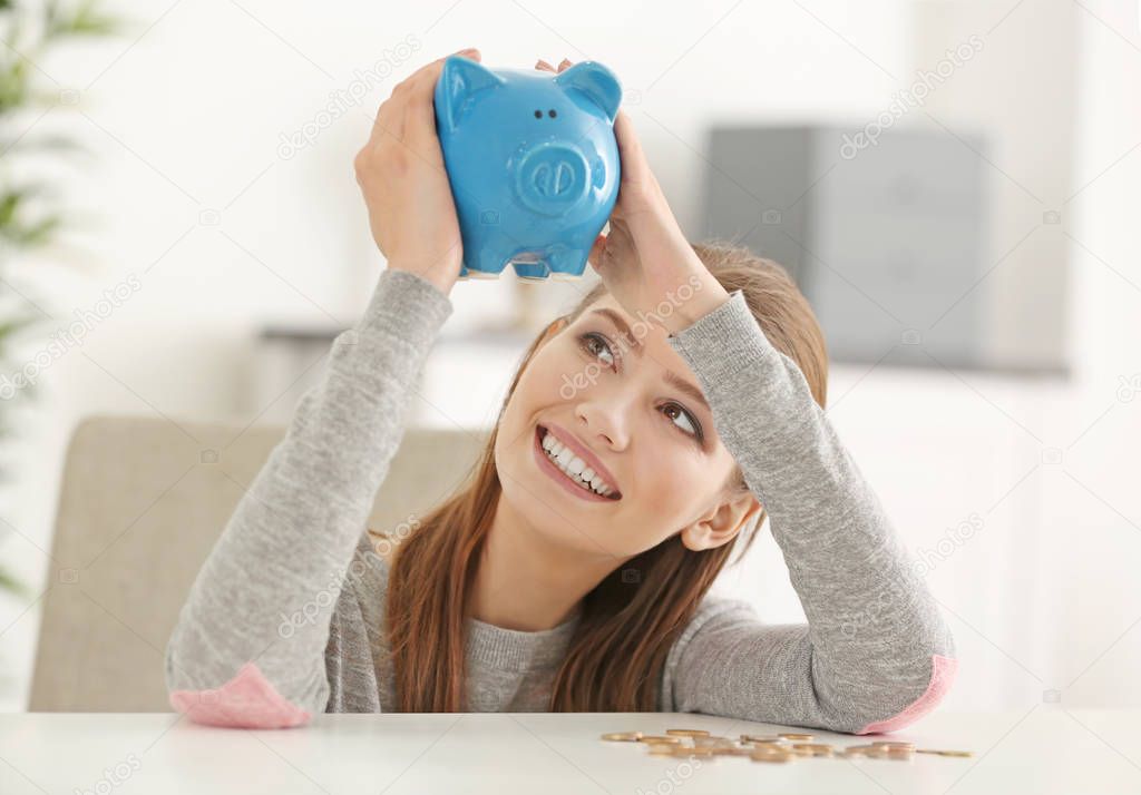 Beautiful young woman with piggy bank and coins at home