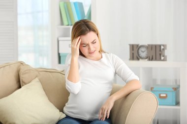 Hamile kadın evde kanepede otururken baş ağrısı acı