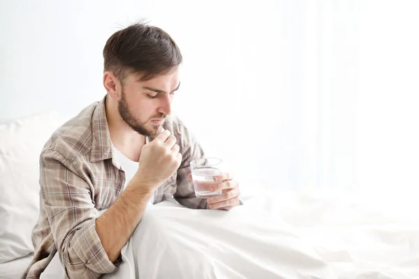 Young man sitting on bed and taking pill — Stock Photo, Image