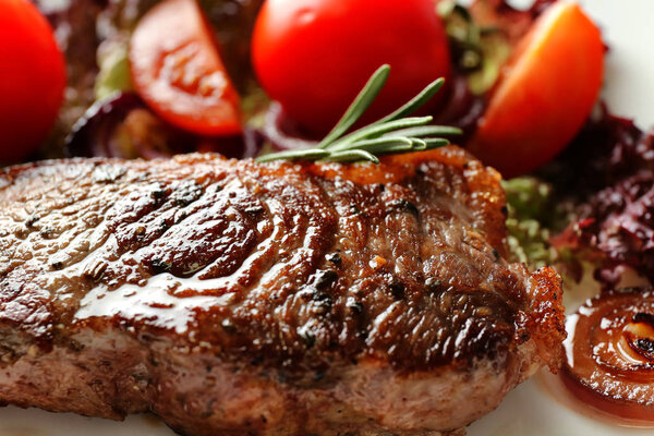 Delicious grilled steak with aromatic rosemary, tomatoes and onion, closeup