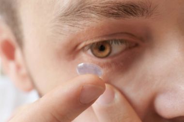 Young man putting contact lens in his eye, closeup clipart