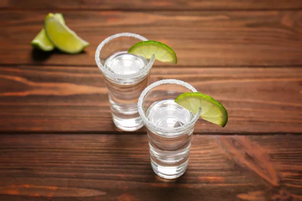 Tequila shots con jugosas rodajas de lima y sal sobre fondo de madera —  Fotos de Stock
