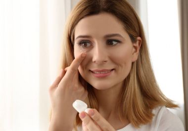 Woman putting contact lenses on light background clipart