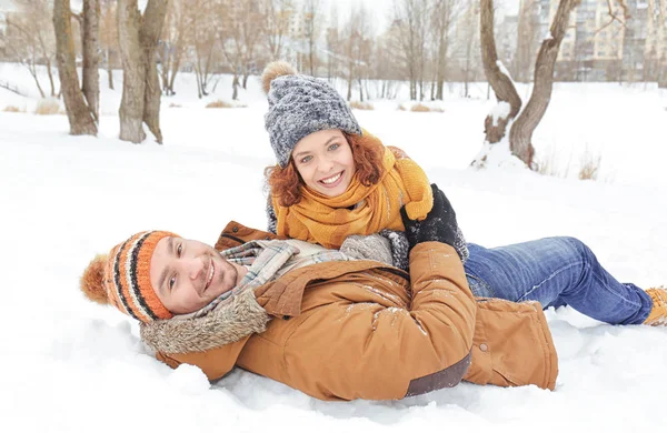 Casal encantador deitado na neve no parque — Fotografia de Stock