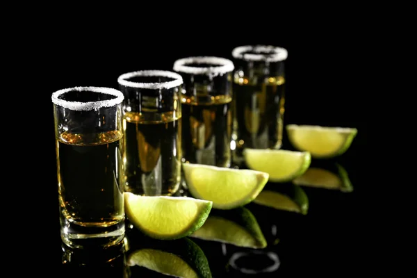 Row of golden tequila shots with juicy lime wedges and salt on black background — Stock Photo, Image