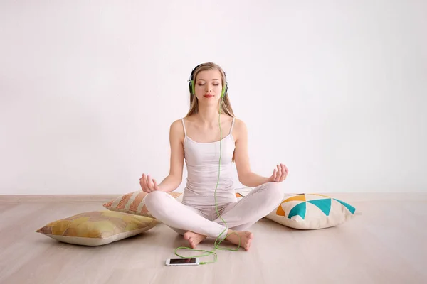 Jovem mulher meditando e ouvindo música enquanto se senta no chão em casa — Fotografia de Stock