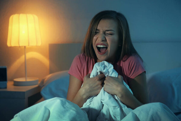 Young scared woman sitting on bed at home