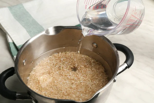 Подача воды в кастрюлю с коричневым рисом на кухонный стол — стоковое фото
