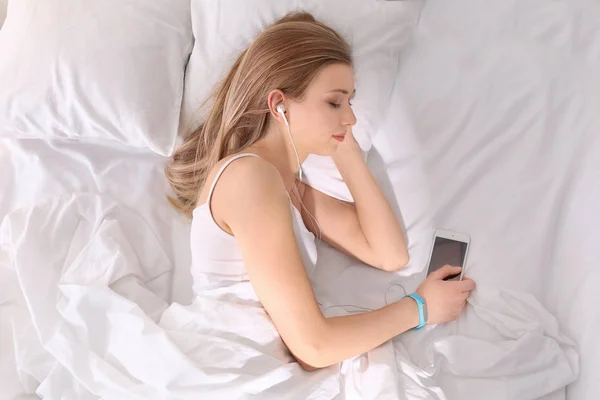 Mujer joven escuchando música mientras descansa en la cama en casa — Foto de Stock