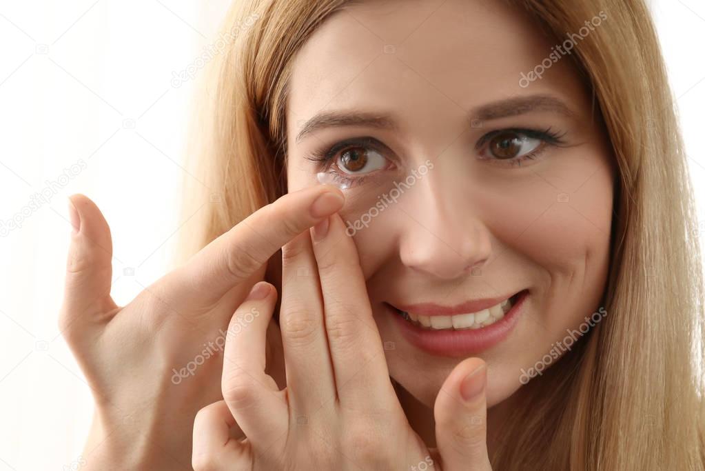 Woman putting contact lenses on white background, closeup