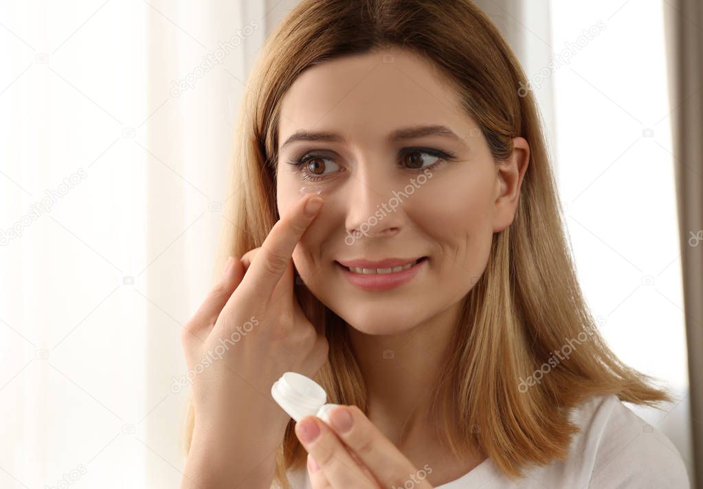 Woman putting contact lenses on light background