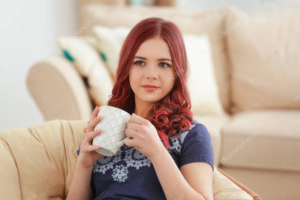Beautiful young woman with dyed hair drinking coffee at home