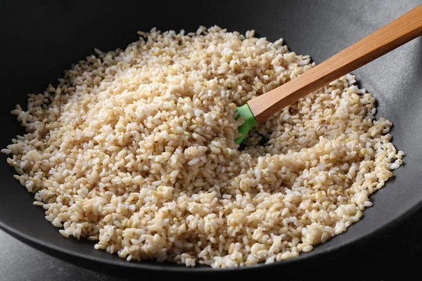 Wok full of brown rice with wooden stirring spoon — Stock Photo, Image