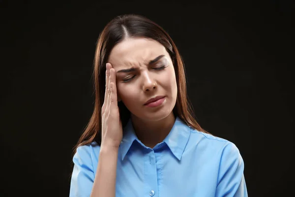 Schöne junge Frau mit Kopfschmerzen auf schwarzem Hintergrund — Stockfoto