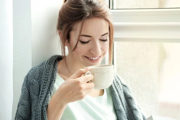 Красива молода жінка п'є чай біля вікна вдома — стокове фото