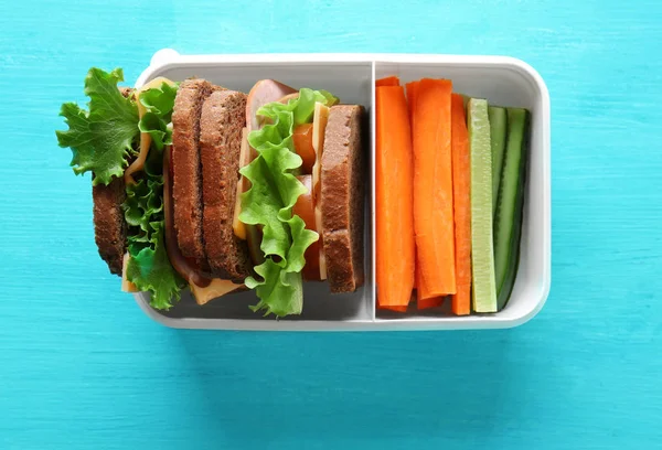 Almuerzo escolar saludable en caja de plástico sobre mesa de madera azul — Foto de Stock