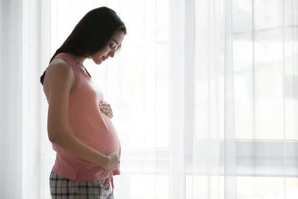 Piękne kobiety w ciąży, stojący w pobliżu okna w domu — Zdjęcie stockowe