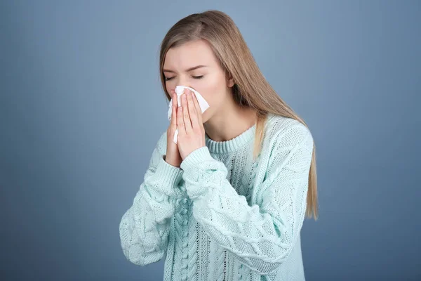 Jonge vrouw blazen neus op weefsel tegen een achtergrond met kleur — Stockfoto