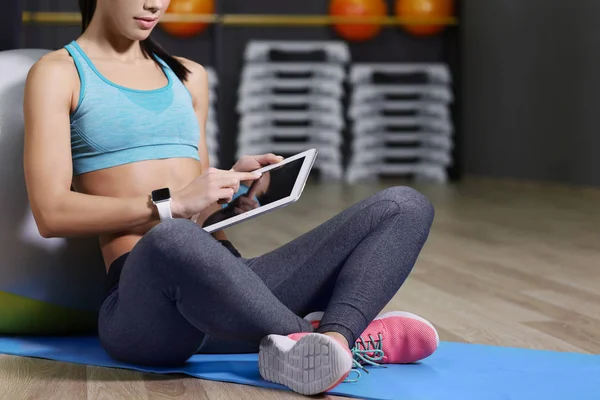 Mladá žena s tabletovým počítačem a fitness tracker v tělocvičně — Stock fotografie