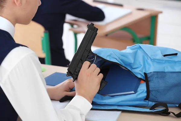 Schoolboy sitting at desk with gun — Stock Photo, Image