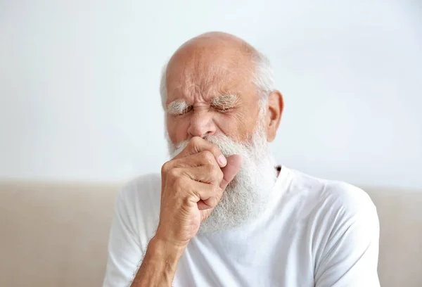 Kašel starší muž sedí na pohovce — Stock fotografie