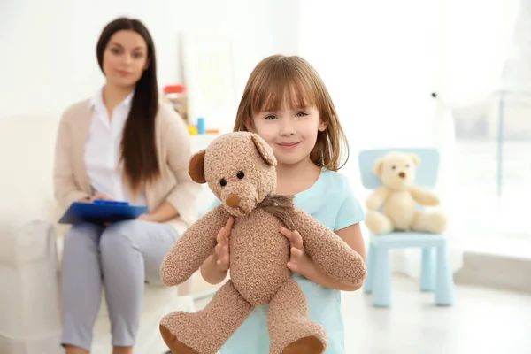 Niña con osito de peluche y psicólogo infantil en segundo plano — Foto de Stock