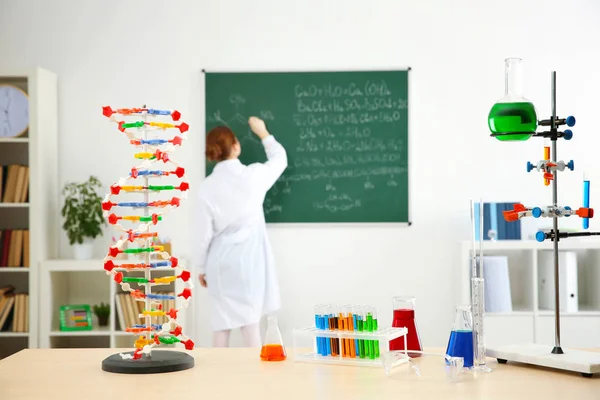 Робоче місце з різними інструментами і шкільна дівчина, що пише на дошці в хімічному класі — стокове фото