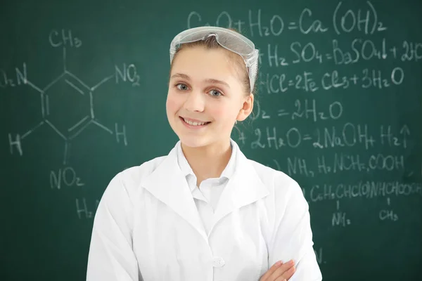 Beautiful school girl standing on chalkboard background in chemistry class — Stock Photo, Image