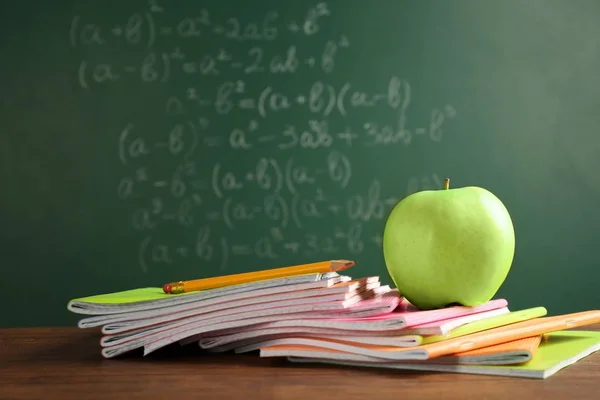 Copybooks and apple on chalkboard background — Stock Photo, Image