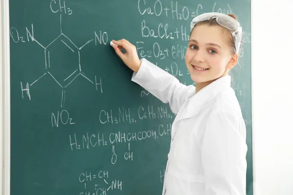 Beautiful school girl standing at chalkboard in chemistry class — Stock Photo, Image