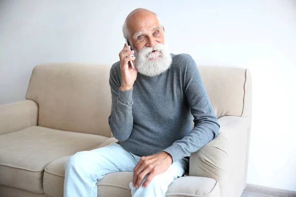 Homem sênior sentado no sofá e falando no celular — Fotografia de Stock