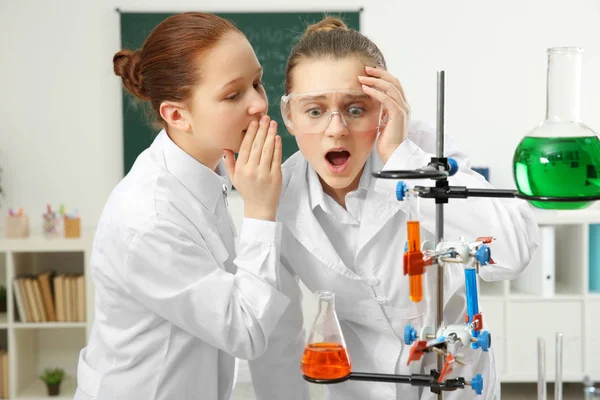 Dos niñas de la escuela susurrando y haciendo experimentos en clase de química — Foto de Stock