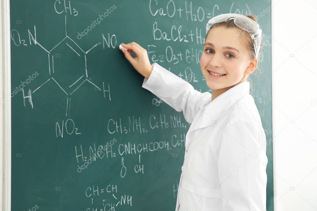 Beautiful school girl standing at chalkboard in chemistry class