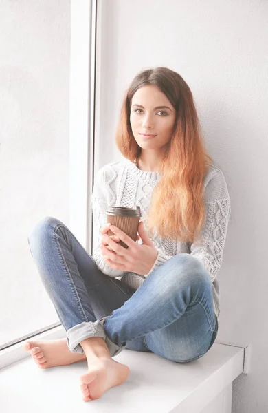 Belle jeune femme buvant du café assis sur le rebord de la fenêtre à la maison — Photo