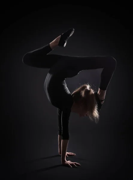 Νεαρή κοπέλα κάνει γυμναστική σε σκούρο φόντο — Φωτογραφία Αρχείου