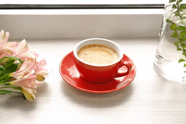 Cup of hot coffee and flowers on window sill — Stock Photo, Image