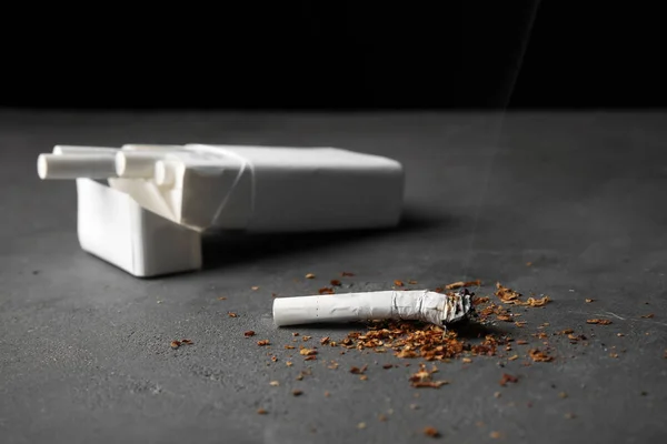 Sigaretta e confezione danneggiati sul tavolo grigio — Foto Stock