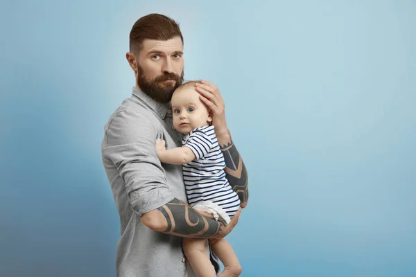 Guapo tatuado joven sosteniendo lindo bebé en fondo claro — Foto de Stock