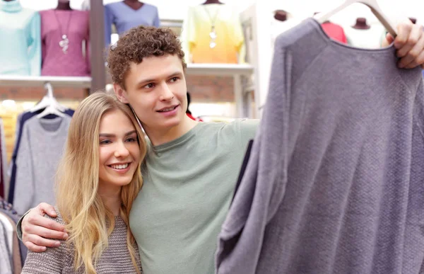 Feliz joven pareja eligiendo ropa en la tienda moderna —  Fotos de Stock